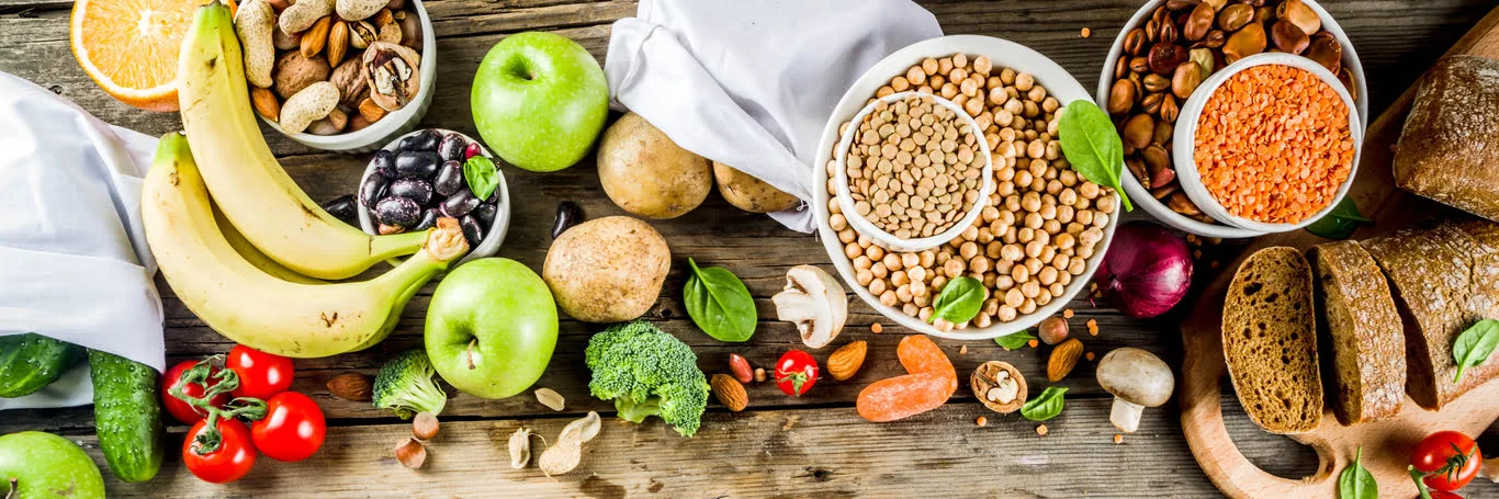 Gesunde Lebensmittel auf Tisch serviert und von oben fotografiert, darunter Vollkornbrot, Erbsen, Nüsse, Trockenfrüchte, Äpfel, Bananen, Tomaten, Gurken usw.